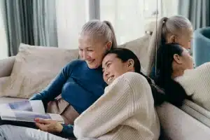Older and younger woman sitting together on a sofa smiling, depicting a healthy and happy intergenerational bond