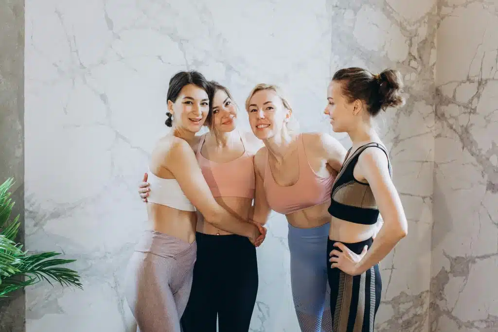 Four smiling women in activewear posing together against a marble wall, promoting health and wellness