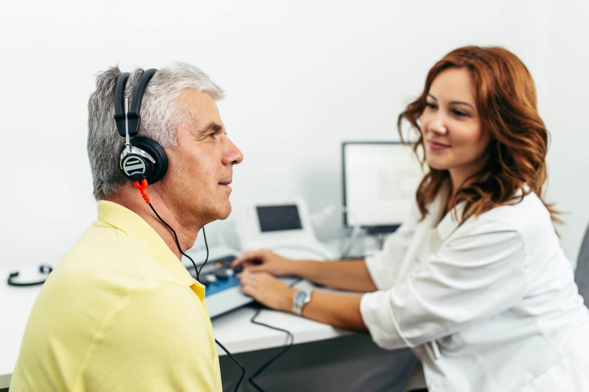 Audiologist conducting a hearing test on an older man wearing headphones in a clinical setting