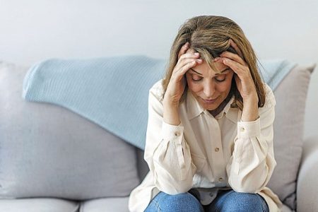Tired woman sitting on a sofa holding her head in her hands, showing signs of fatigue and exhaustion